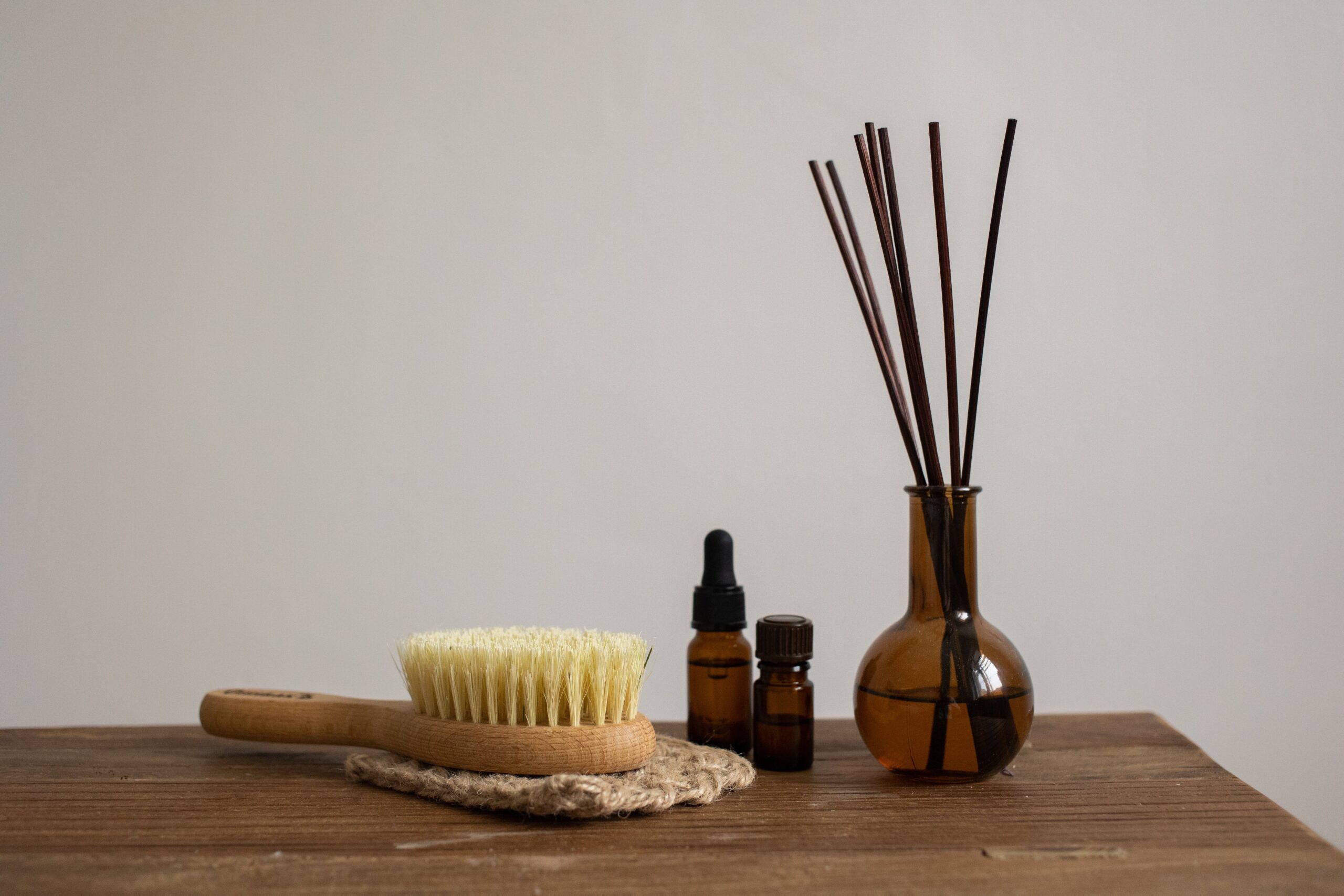 Minimalist aromatherapy set with essential oils, brush, and diffuser sticks on wooden table.